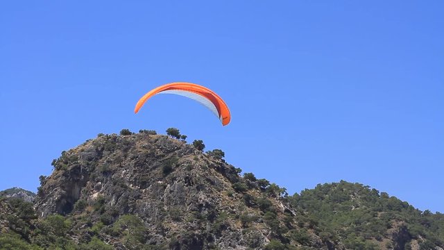 Red and white colored paraglider, airborne in a clear blue sky. Two people paragliding in tandem. Landing at Oludeniz Beach after taking off from Babadag mountain 1600 meters above sea level in Turkey
