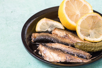 
 Snack. Sprats and lemon slices on a small black plate.