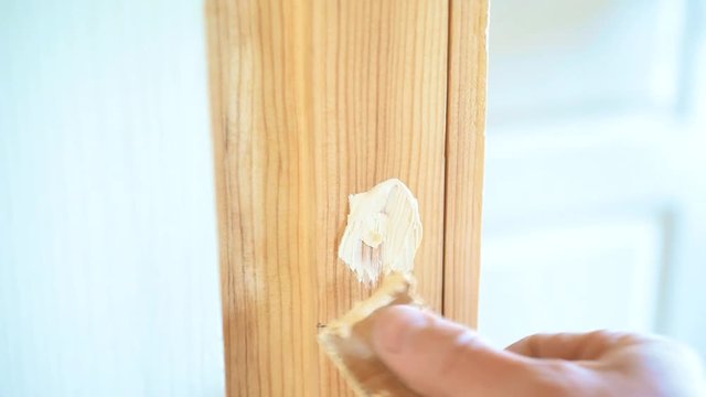 Close-up of hand spackling a round countersunk hole with screw head in door frame by filling the hollow cavity in wood with putty