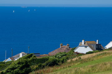 Fototapeta na wymiar Houses on the southern coast of Devon. On a hill on the background of the sea. Sailboats are visible in the distance. England