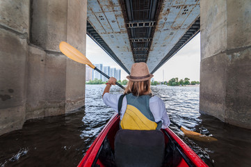 Meeting morning on kayaks. Rear view of young girl kayaking bu the river and under the bridge. Urban exploration concept