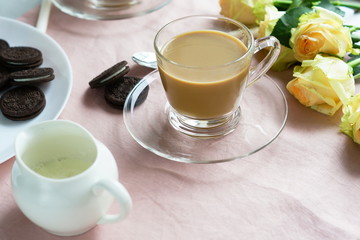 Tea with milk in a glass cup and cookies on a pink background