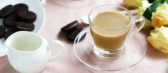 Tea with milk in a glass cup and cookies on a pink background