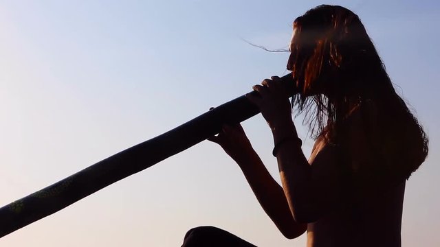 Didgeridoo playing. Male Silhouette with Didgeridu near Sea.