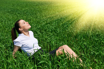Business woman relaxing in green grass field outdoor under sun. Beautiful young girl dressed in suit resting, spring landscape, bright sunny day