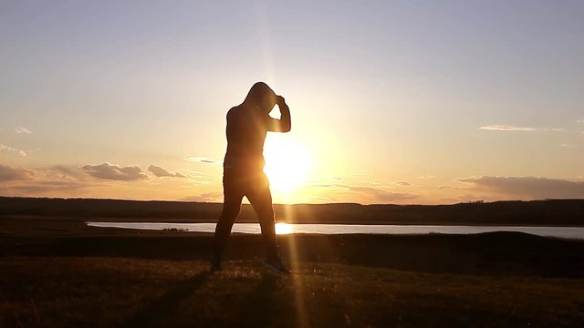Silhouette of man exercising thai boxing. Silhouette of martial arts man training boxing on the beach over beautiful sunset background. Training karate or boxing on grass field at sunset.
