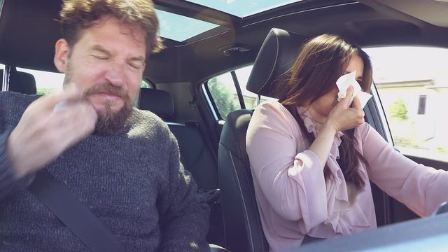 Couple driving car sneezing with strong allergy for spring with pollen in car