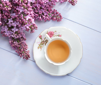 Cup of tea  and branches of blooming lilac on  wooden table.