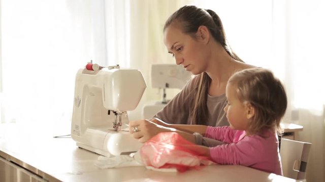Young attractive mother working on sewing machine with her little cute daughter