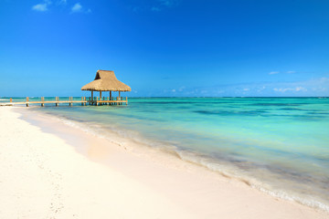 Tropical white sandy beach. Palm leaf roofed wooden pier with gazebo on the beach. Punta Cana, Dominican Republic