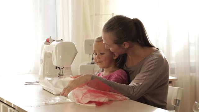 Young attractive mother working on sewing machine with her little cute daughter
