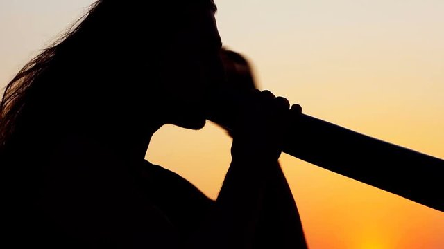 Didgeridoo playing. Male Silhouette with Didgeridu near Sea.