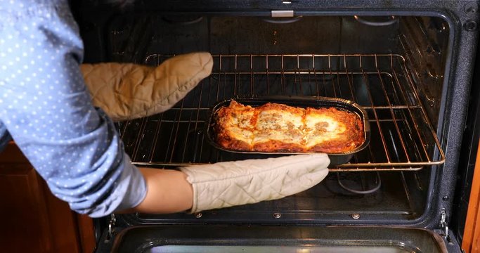 Female gloved hands taking out freshly baked lasagna from oven