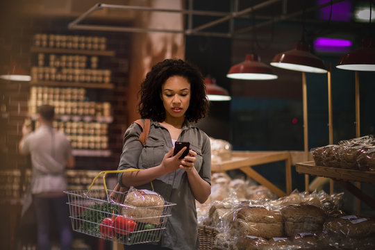 Woman late night grocery shopping and using smartphone