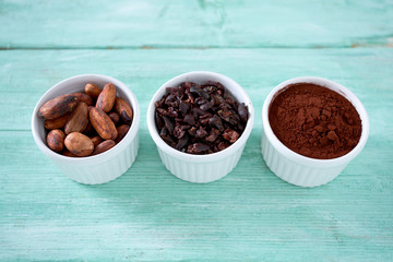 cocoa nibs, beans and powder on turquoise surface