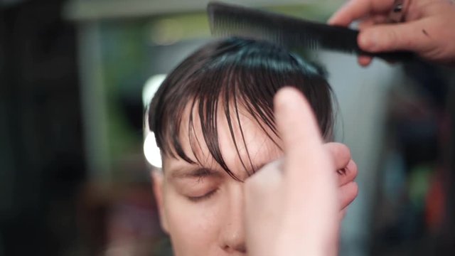 Barber with dark hair and tattoo doing a haircut for brutal client with scissors at barber shop. Slow motion.