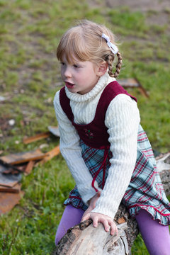 A little girl in a dress plays near a fallen tree near a lake.