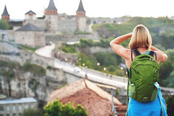 Naklejka premium Woman tourist with green backpack makes a photo of an old castle. vacation and summer trip