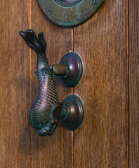Old wooden door to house with a brass knocker in the shape of a fish and a bull`s eye, sea element