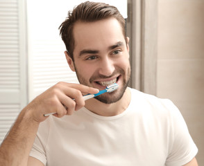 Handsome man brushing teeth in bathroom