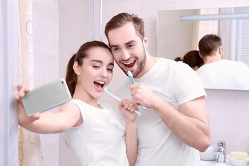 Young happy couple taking selfie while brushing teeth in bathroom