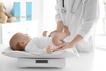 Female doctor weighting cute baby in clinic