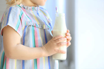 Cute little girl with bottle of yogurt at home, closeup