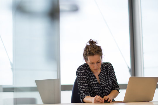 Female executive syncing smartphone to laptop