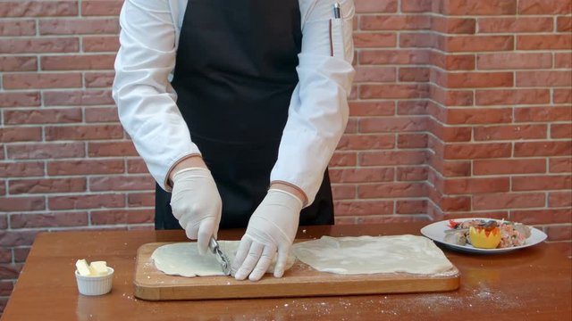 Chef hads slicing dough sheet with roller knife