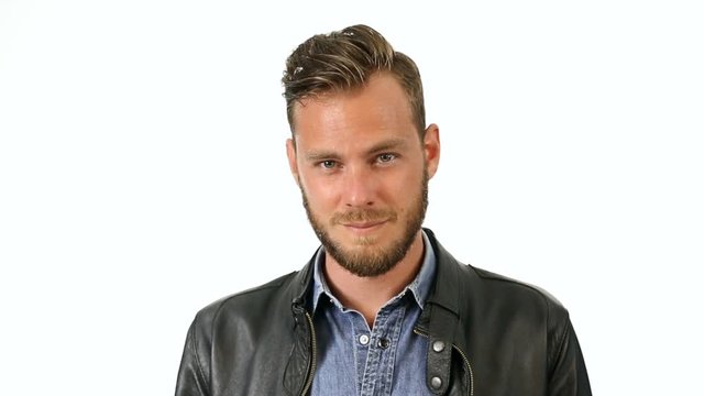 Attractuve man in a black leather jacket and jeans shirt, standing gesturing against a white background with a smile.