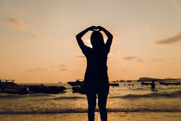 silhouette of a happy young woman on sunset, Beautiful woman hands making a heart shape with sea background on sunset