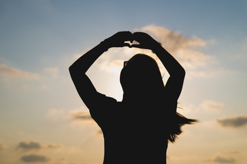 silhouette of a happy young woman on sunset, Beautiful woman hands making a heart shape with sea background on sunset