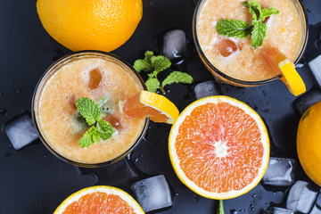 Fresh orange juice, mint and ice on dark background, top view