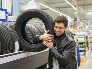 Fototapeta na wymiar Glad male customer buying new tires in the supermarket. He looks happy