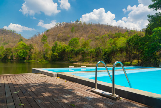 Blue swimming pool with wooden flooring near the lake mountain and tree with blue sky