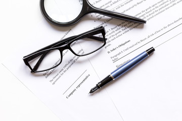 Pen and glasses lying on signed documents on office desk top view