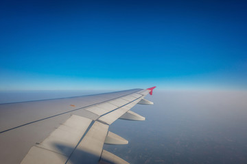 Wing of airplane flying above the clouds and blue sky.