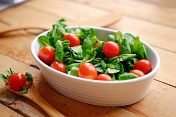 Cherry tomatoes and basil salad in a white cup on a wooden table.