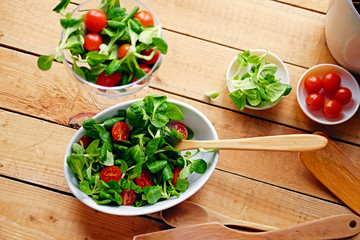 Cherry tomatoes and basil salad on a plate with a pot on a wooden table.