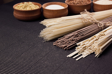 Raw japanese noodles with ingredient in wooden bowls on black striped mat background with copy space.