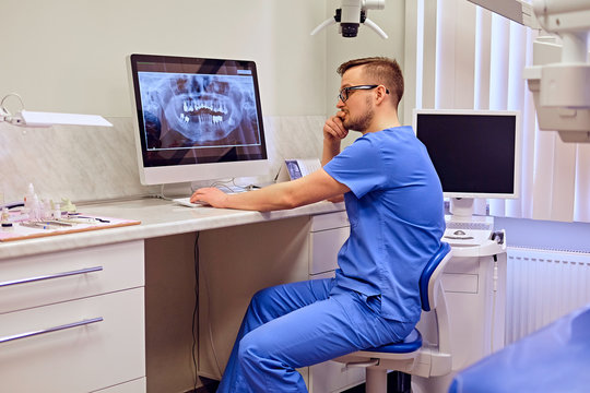 Male dentist looking at teeth x-ray on the computer in a dentist office.