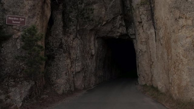 FPV CLOSE UP: Driving through narrow passage in rocky granite wall called Needle's Eye Tunnel and exiting on stone ledge with scenic overlook over the Black Hills National Forest reserve, South Dakota