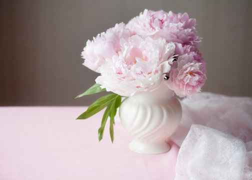 Light pink double Peonies in white ceramic vase, lace and copy space.