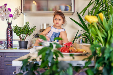 A cute little girl sits on a table in a kitchen and try to make diet porridge.
