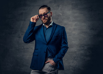 A stylish bearded male dressed in a suit and sunglasses over dark grey background.