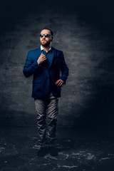 Full body studio portrait of stylish bearded male dressed in a suit and sunglasses.