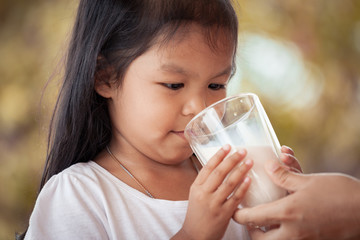 Asian little girl try to drink a milk from glass she don't like it