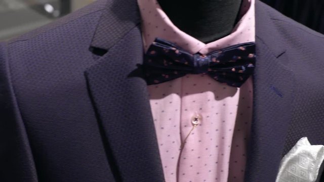 PAN of glass case of menswear boutique with collection of expansive fashionable bowties, and then focus on mannequin in suit and bowtie
