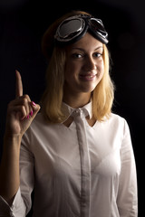 Portrait of young and attractive, blond woman close up on black background with huge glasses on het forehead and raised index finger up.