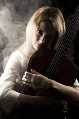 Portrait of young and attractive, blond woman close up on black background with guitar and abstract smoke around her.